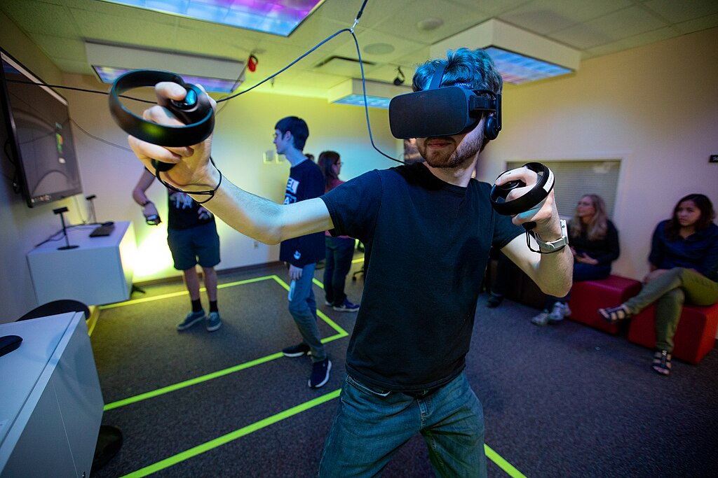A player using the Oculus Rift, a virtual reality headset, and associated controllers to control a game. Photo by Geofflambeth. A player using the Oculus Rift, a virtual reality headset, and associated controllers to control a game. Photo by Geofflambeth.